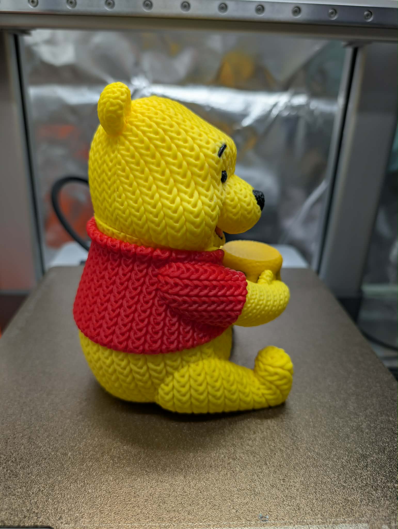 Yellow teddy bear with a red sweater on a metallic surface
