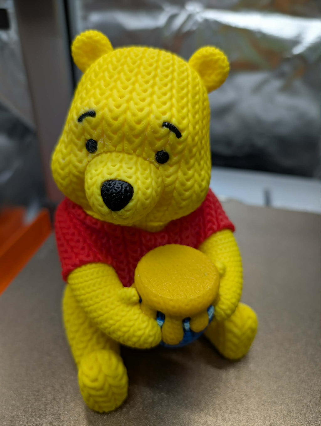 Yellow teddy bear plush toy with a red shirt on a neutral background