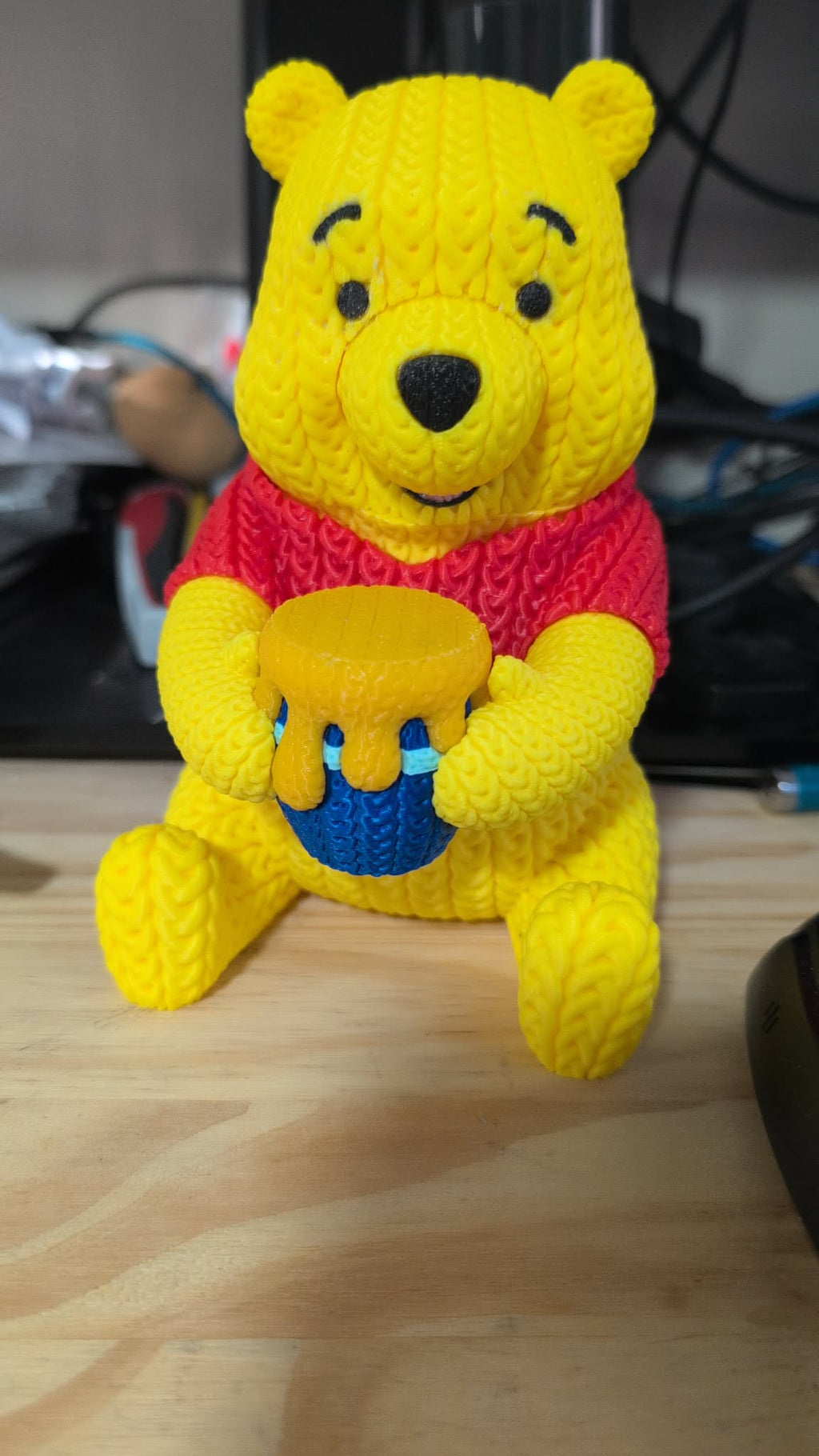 Yellow teddy bear plush toy with a red sweater on a wooden surface.