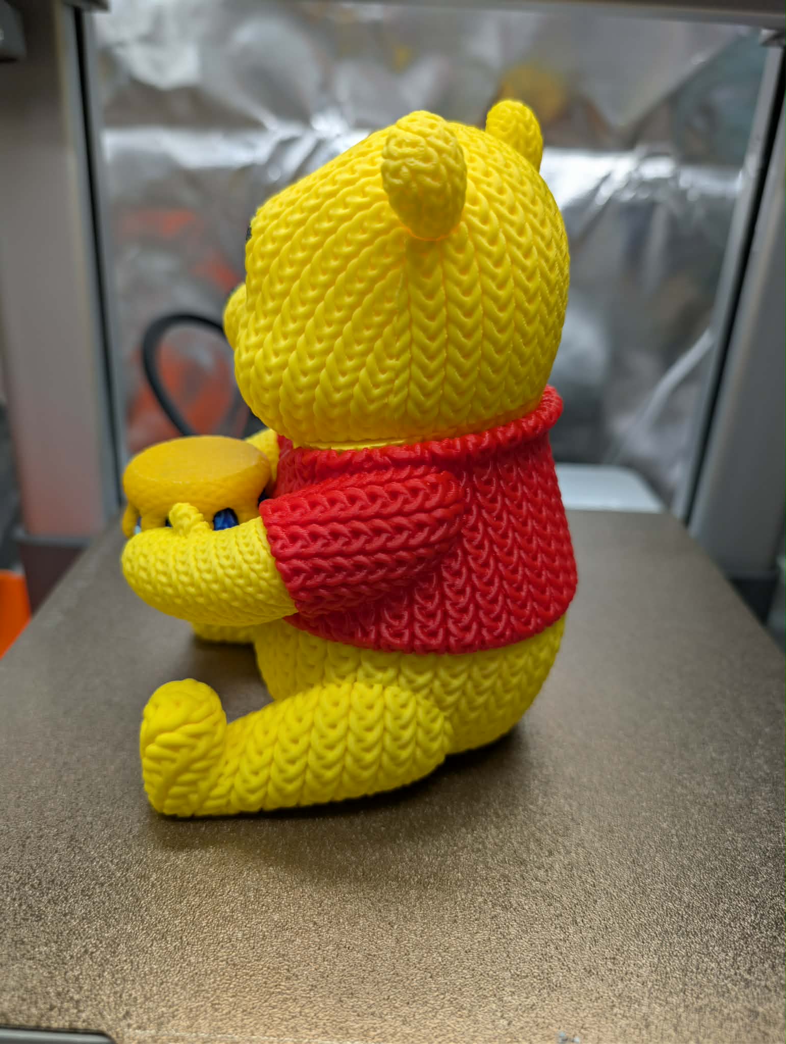 Yellow teddy bear with a red sweater on a metallic surface