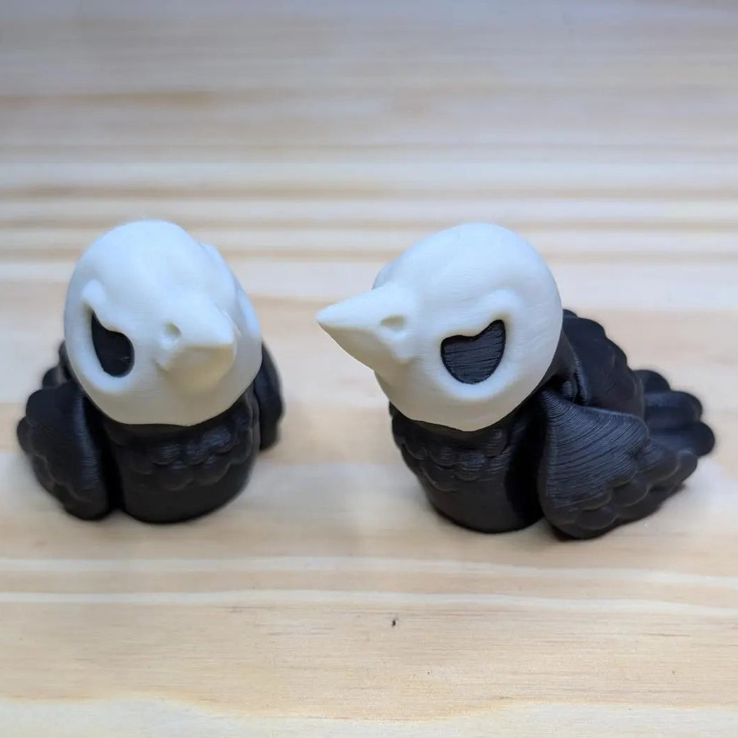 Two bird-shaped objects with black bodies and white faces on a wooden surface