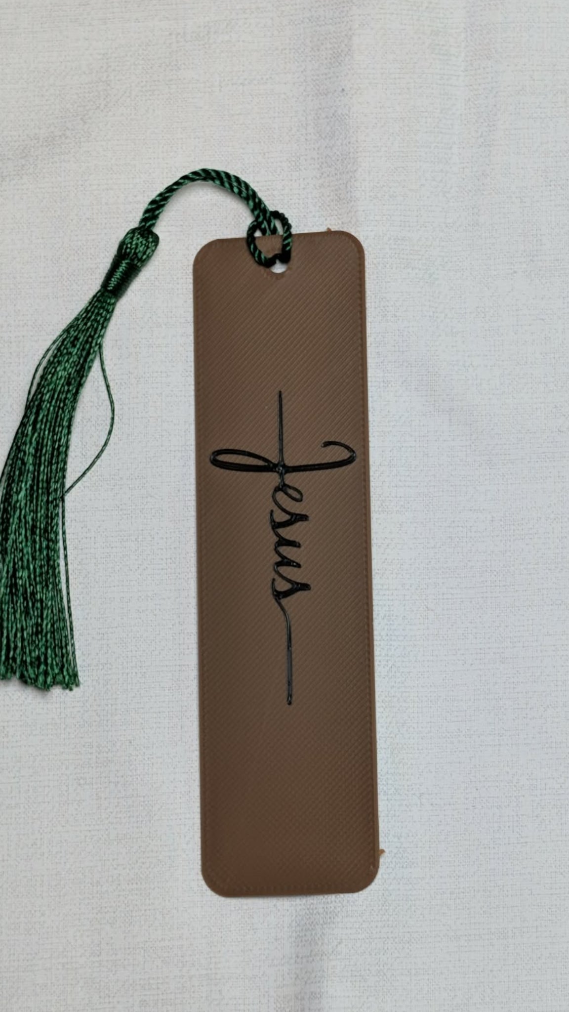 Brown bookmark with 'Jesus' text and green tassel on a light gray background