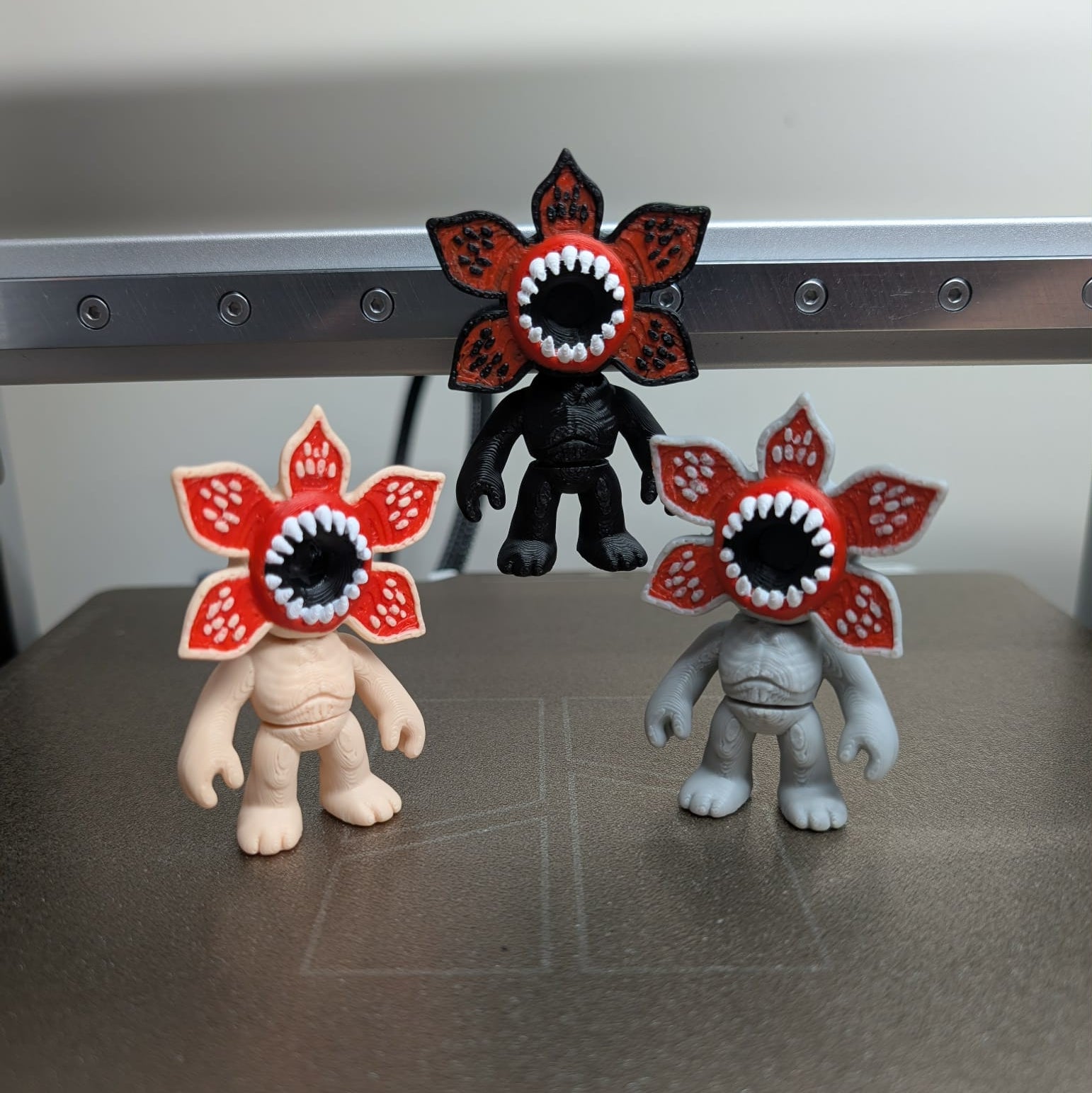 Three small figurines with flower heads featuring sharp teeth on a metallic surface.