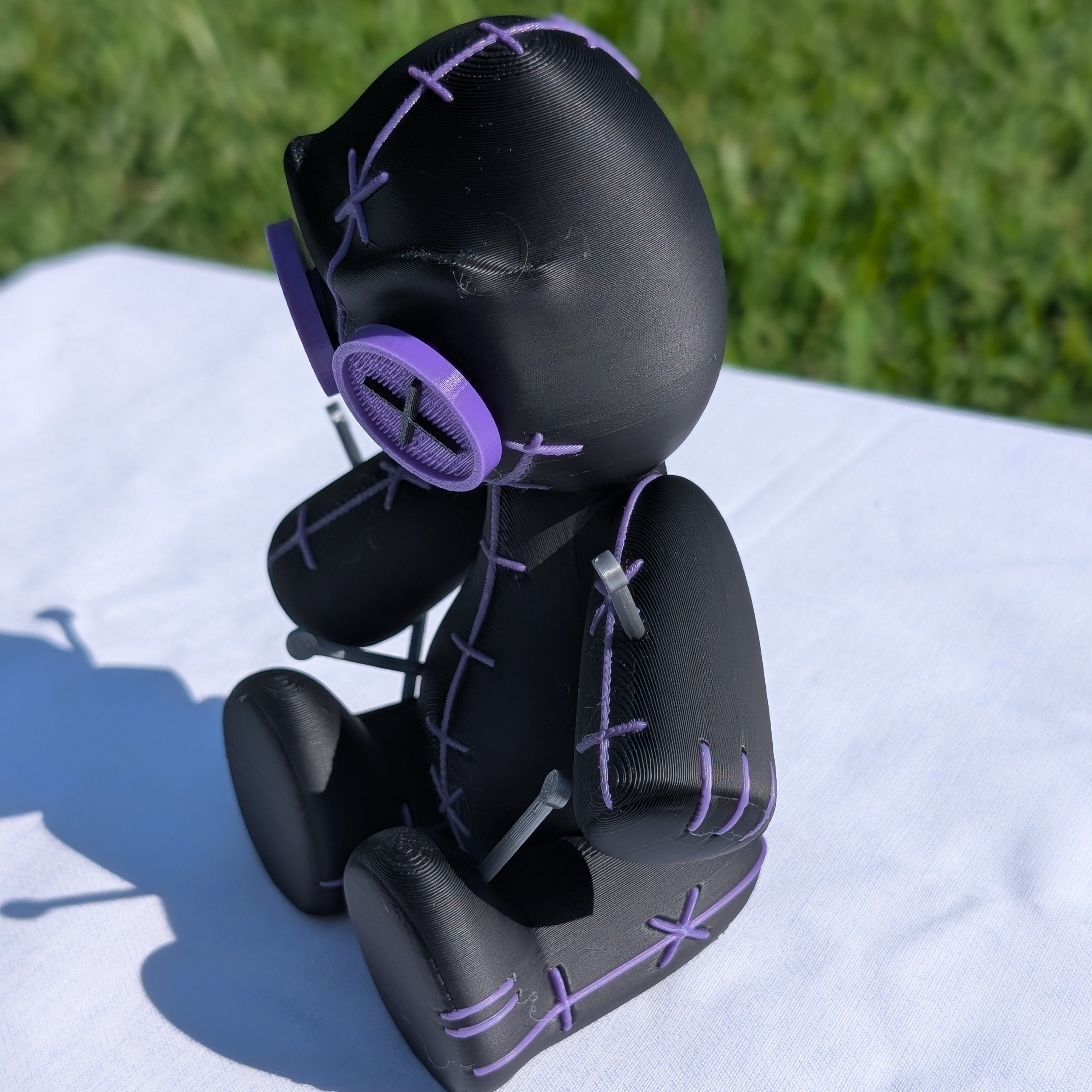 Black and purple toy figure on a white surface with grass in the background