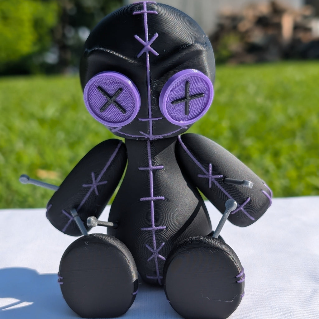 Black and purple plush toy with cross symbols on a white surface with a grassy background