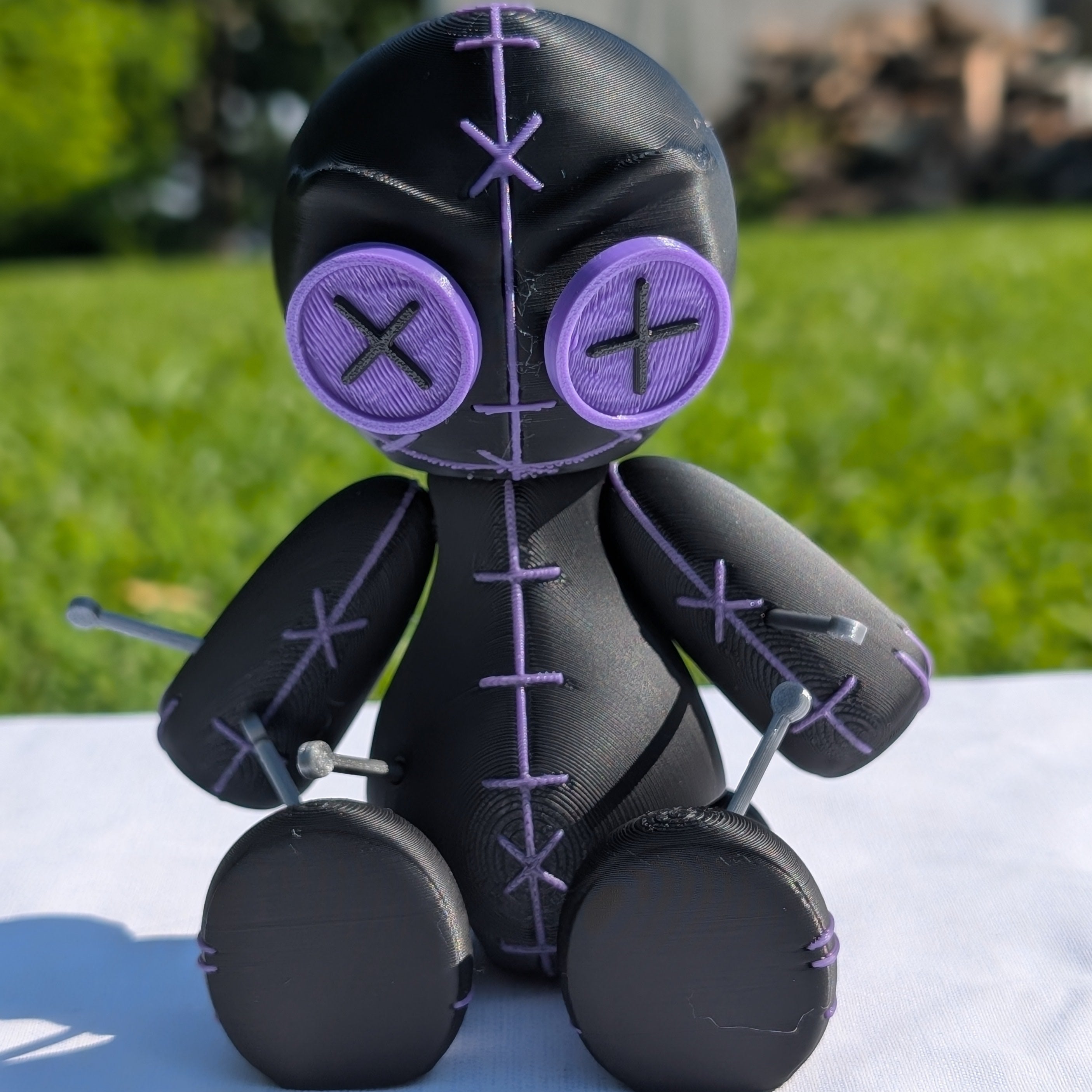 Black and purple plush toy with cross symbols on a white surface with a grassy background