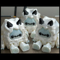 Three white creature figurines with black horns and blue faces on a gray surface.