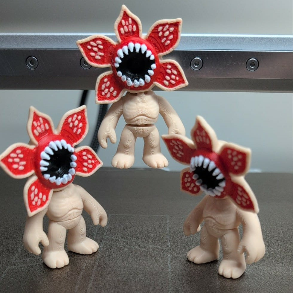 Three small figurines with flower-like heads on a metallic surface