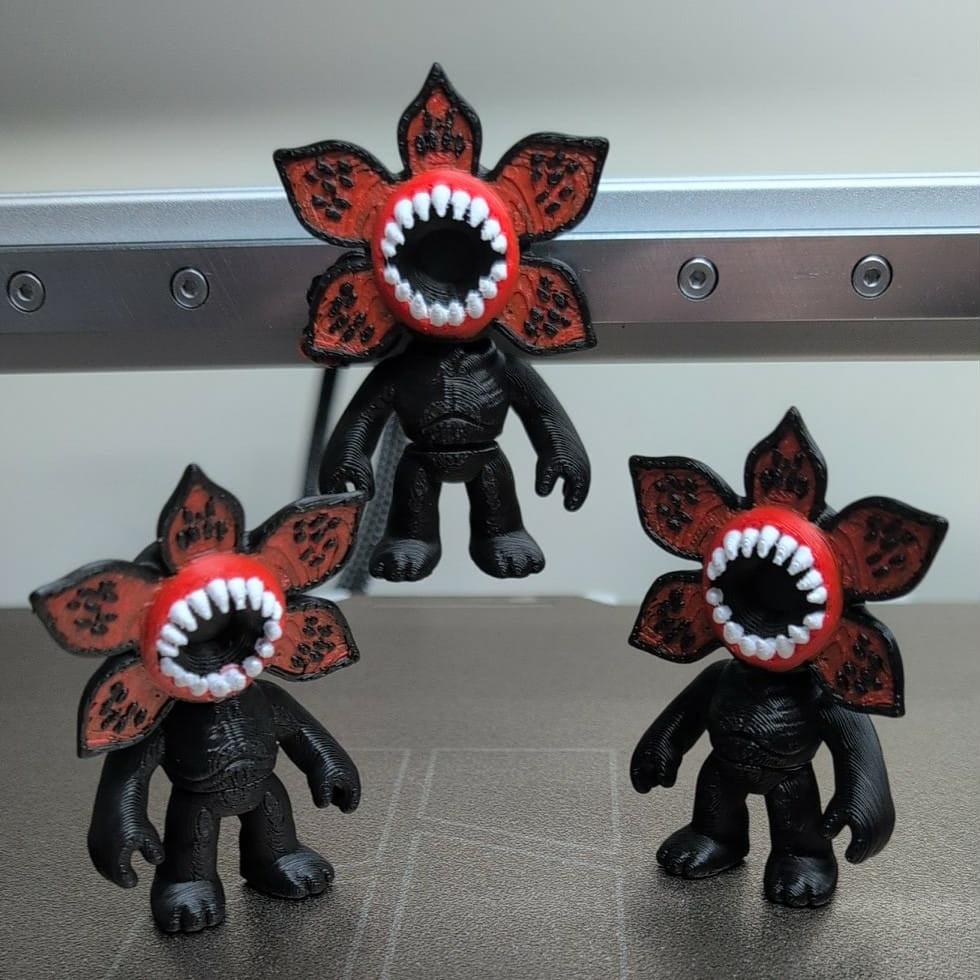 Three black figures with red flower-like heads featuring teeth on a metallic surface.