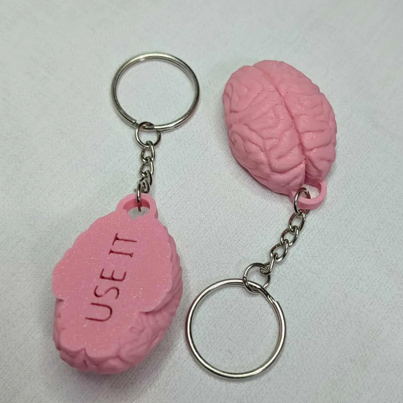 Pink brain-shaped keychains with 'USE IT' text on a light gray background