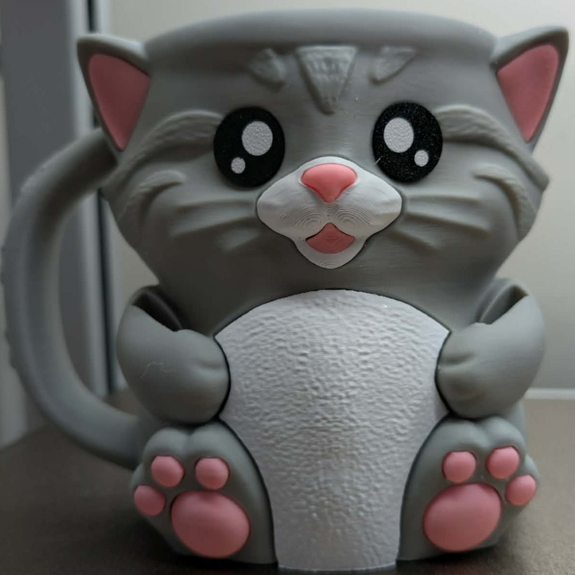 Gray cat-shaped figurine with pink paws on a neutral background