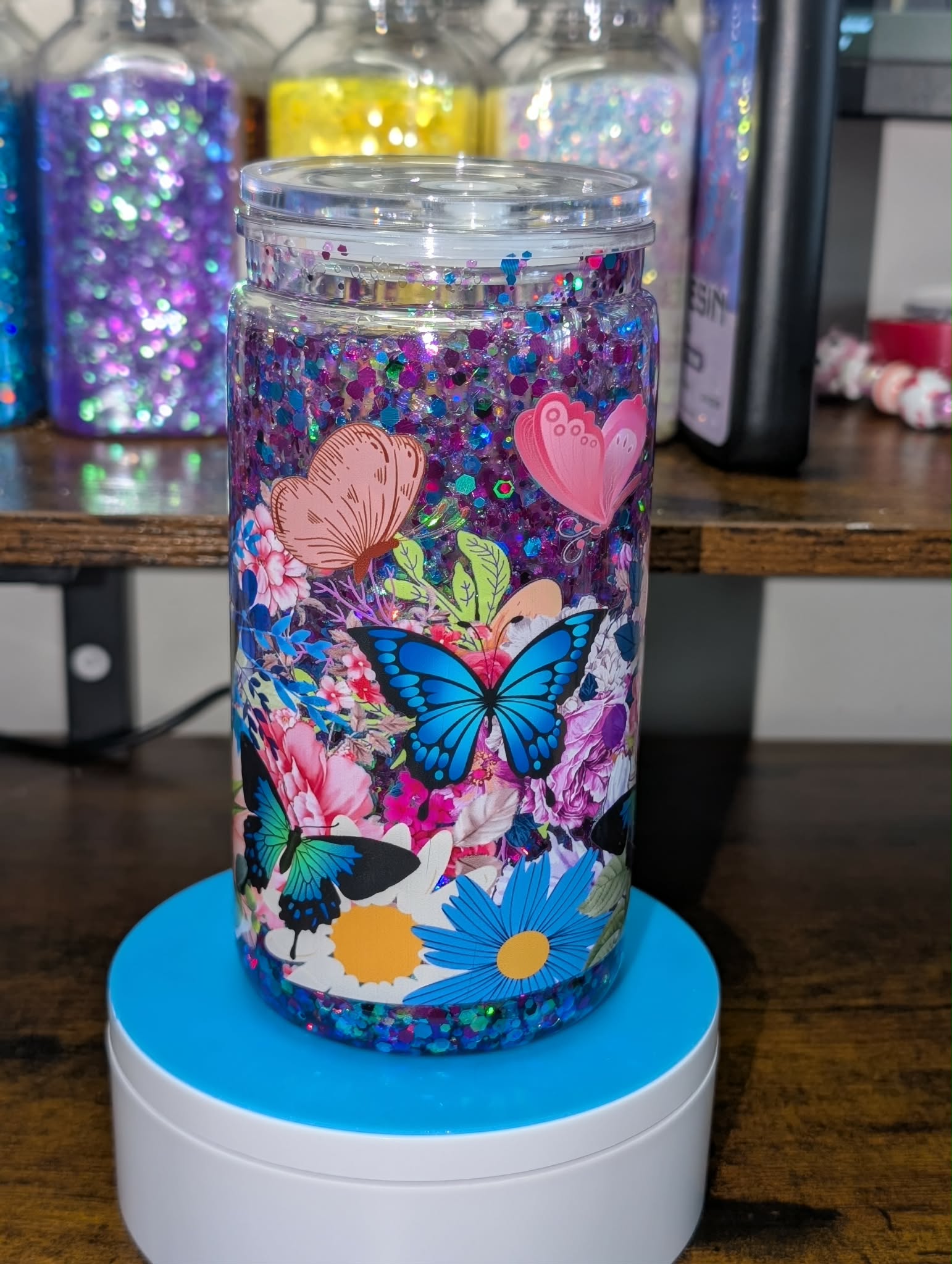 Colorful glittery tumbler with butterfly and floral design on a wooden surface.