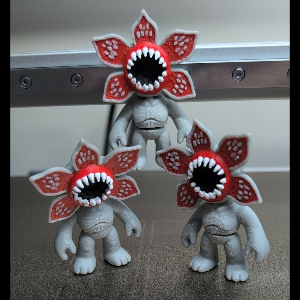 Three toy figures with red and white flower heads and sharp teeth on a metallic surface.