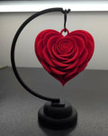 Red heart-shaped rose on a black stand against a neutral background