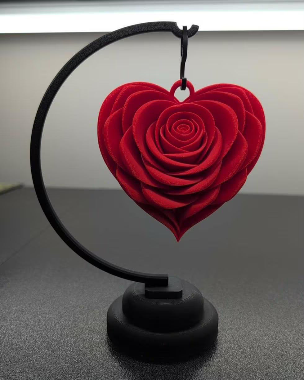 Red heart-shaped rose on a black stand against a neutral background