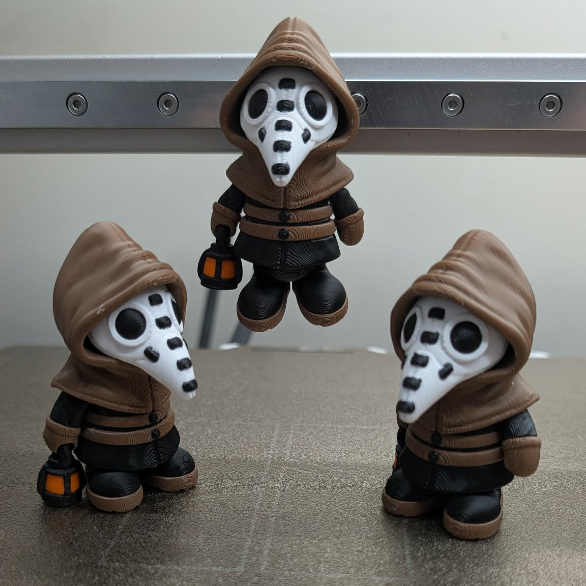 Three identical action figures with hoods and masks on a metallic surface.