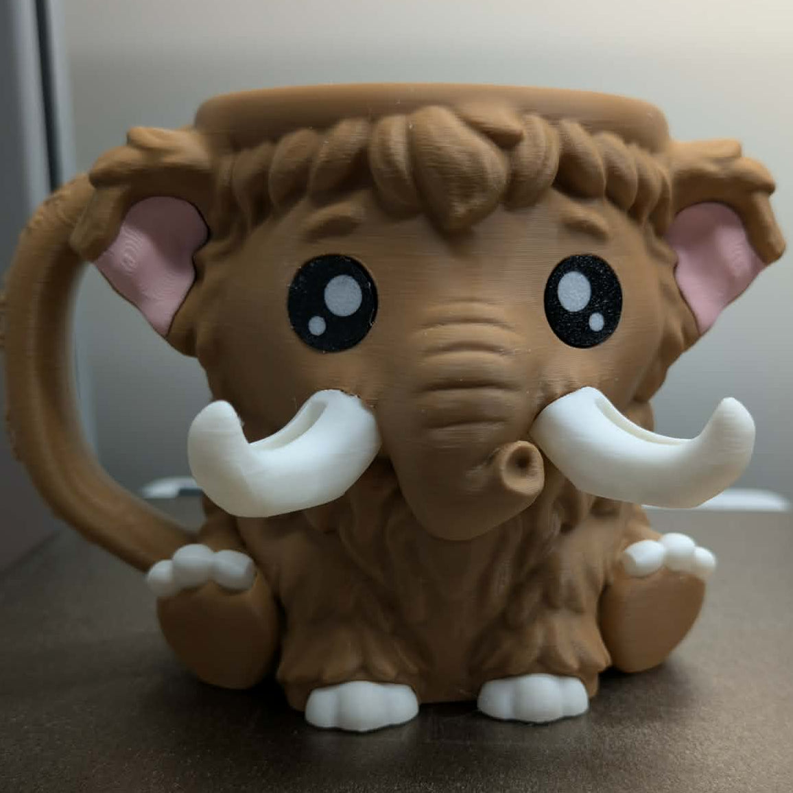 Brown elephant-shaped mug with large tusks on a neutral background