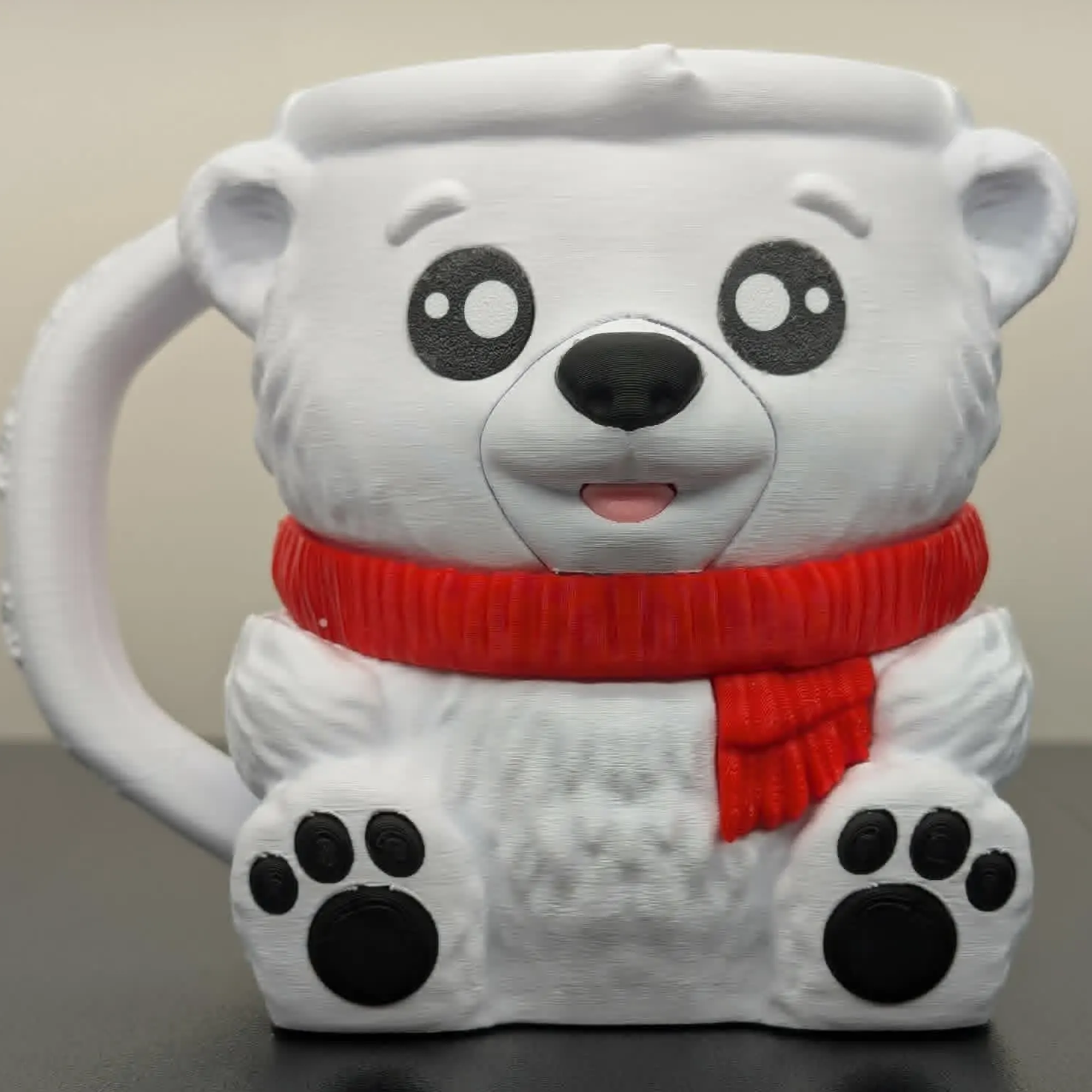 Polar bear-shaped mug with a red scarf on a dark surface.