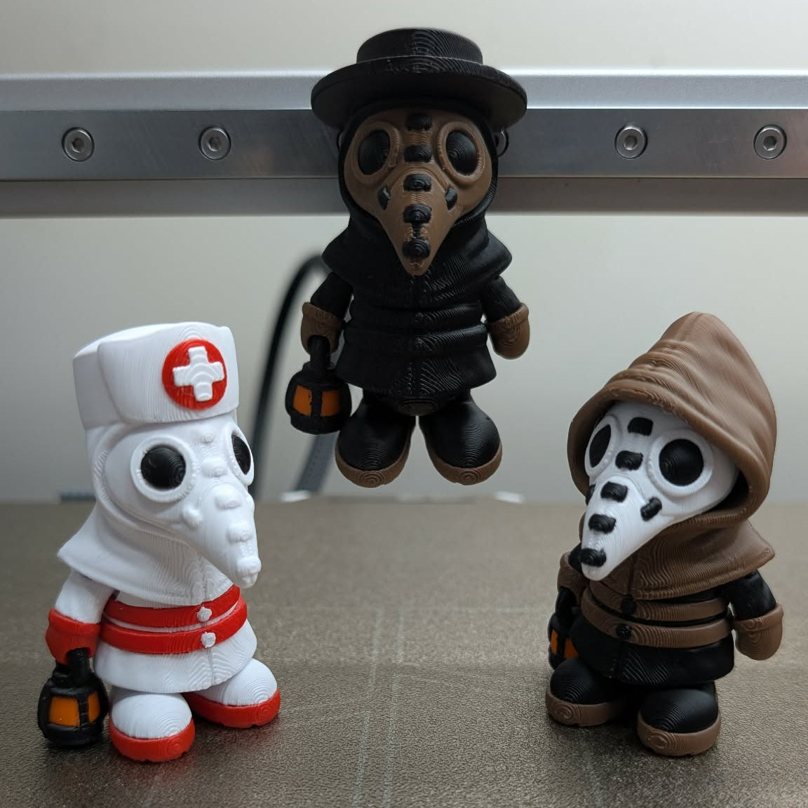Three toy figures of a nurse, a masked character, and a hooded figure on a metallic surface.
