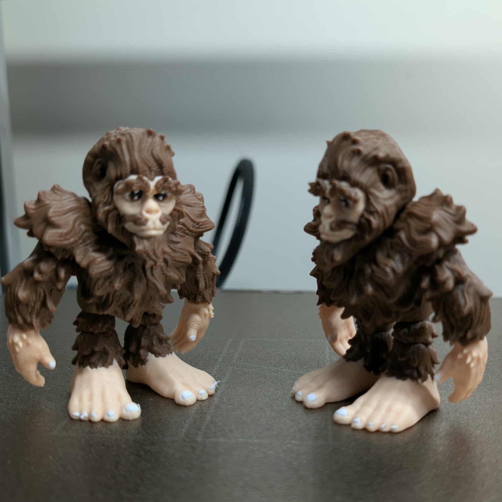 Two toy figures resembling a creature with brown fur and white feet on a dark surface.