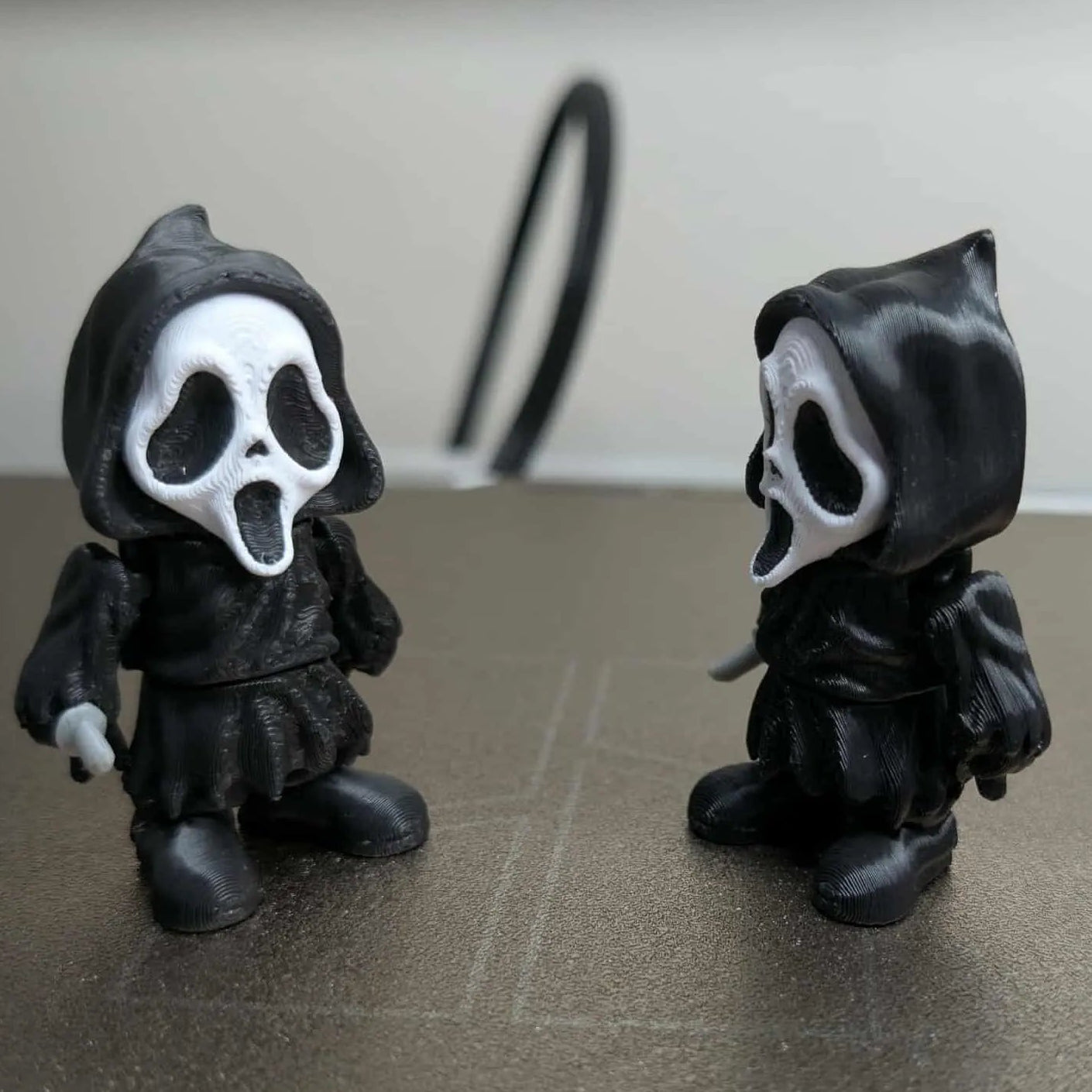 Two black hooded figures with white face masks on a reflective surface.