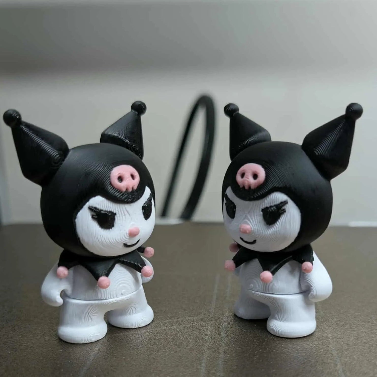 Two small figurines with black hats and pink noses on a reflective surface.