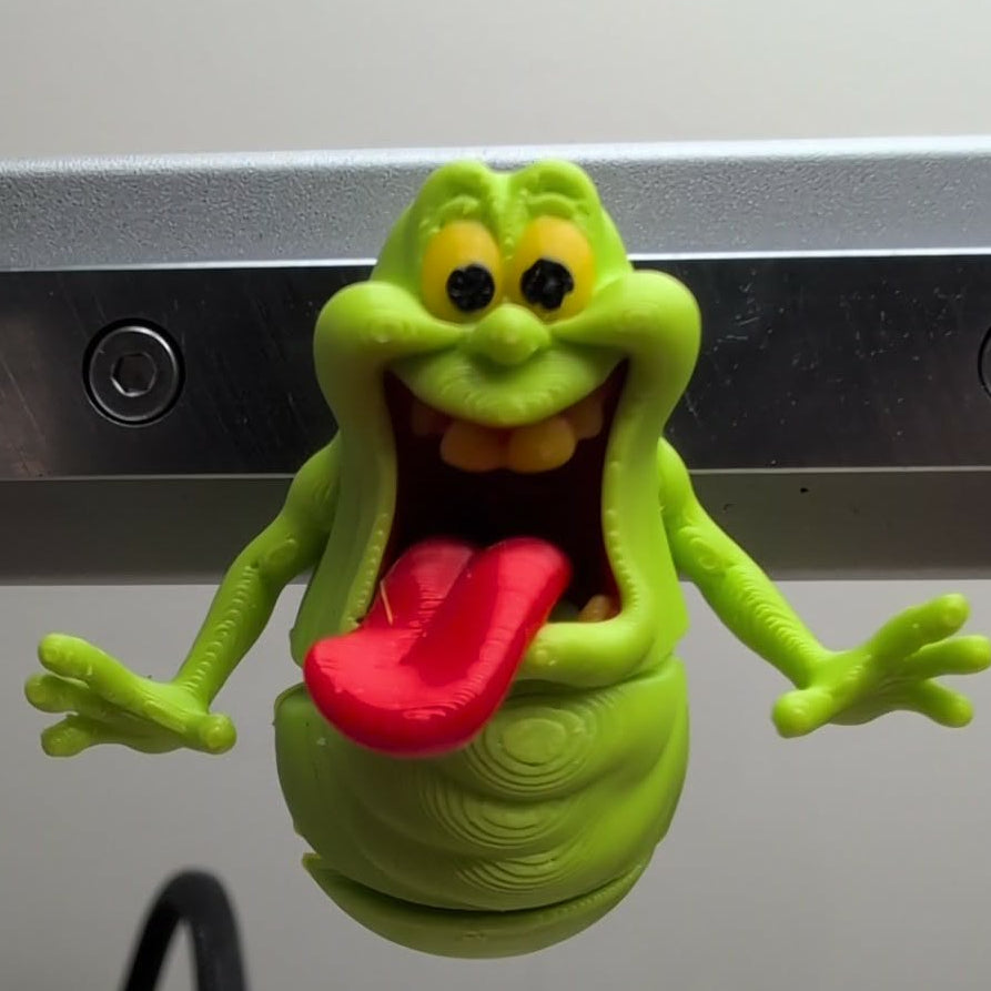 Green cartoon-like creature with a wide open mouth on a metallic surface