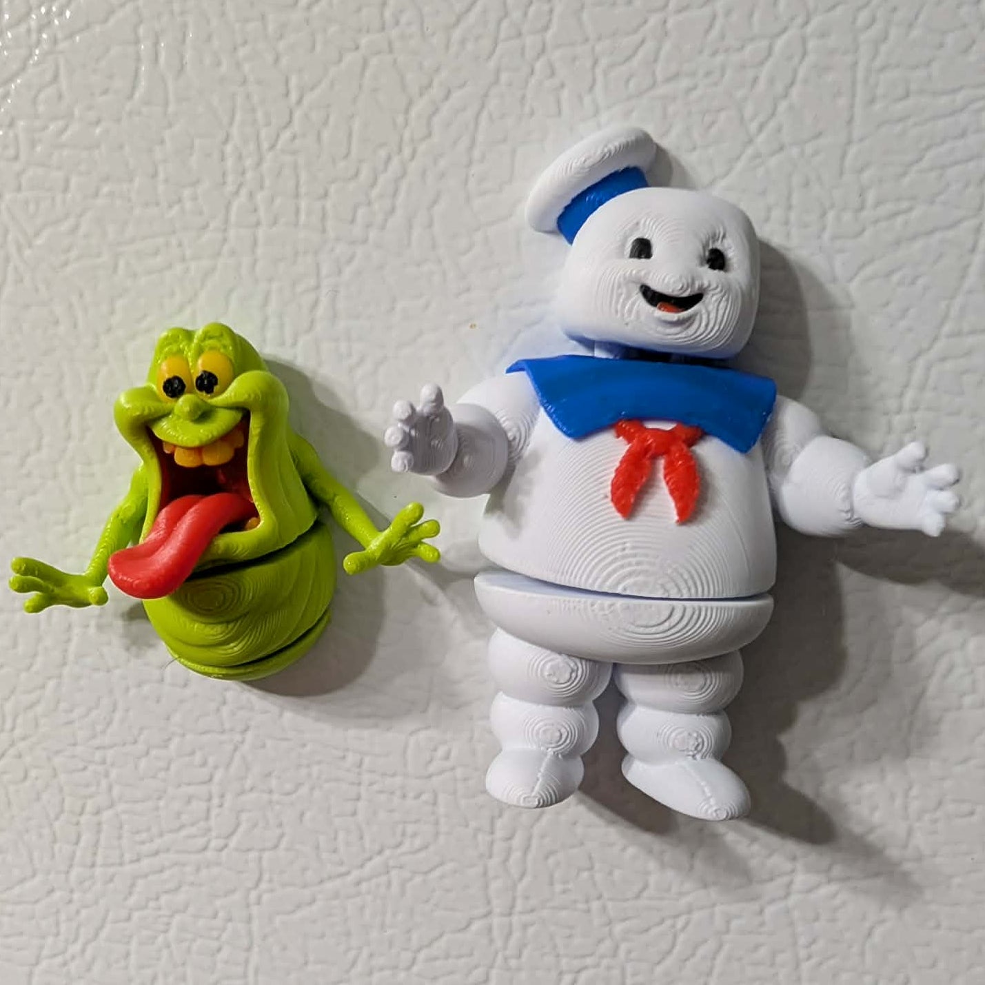Two toy figures on a textured white surface, one green ghost and one white character with a blue bow tie.