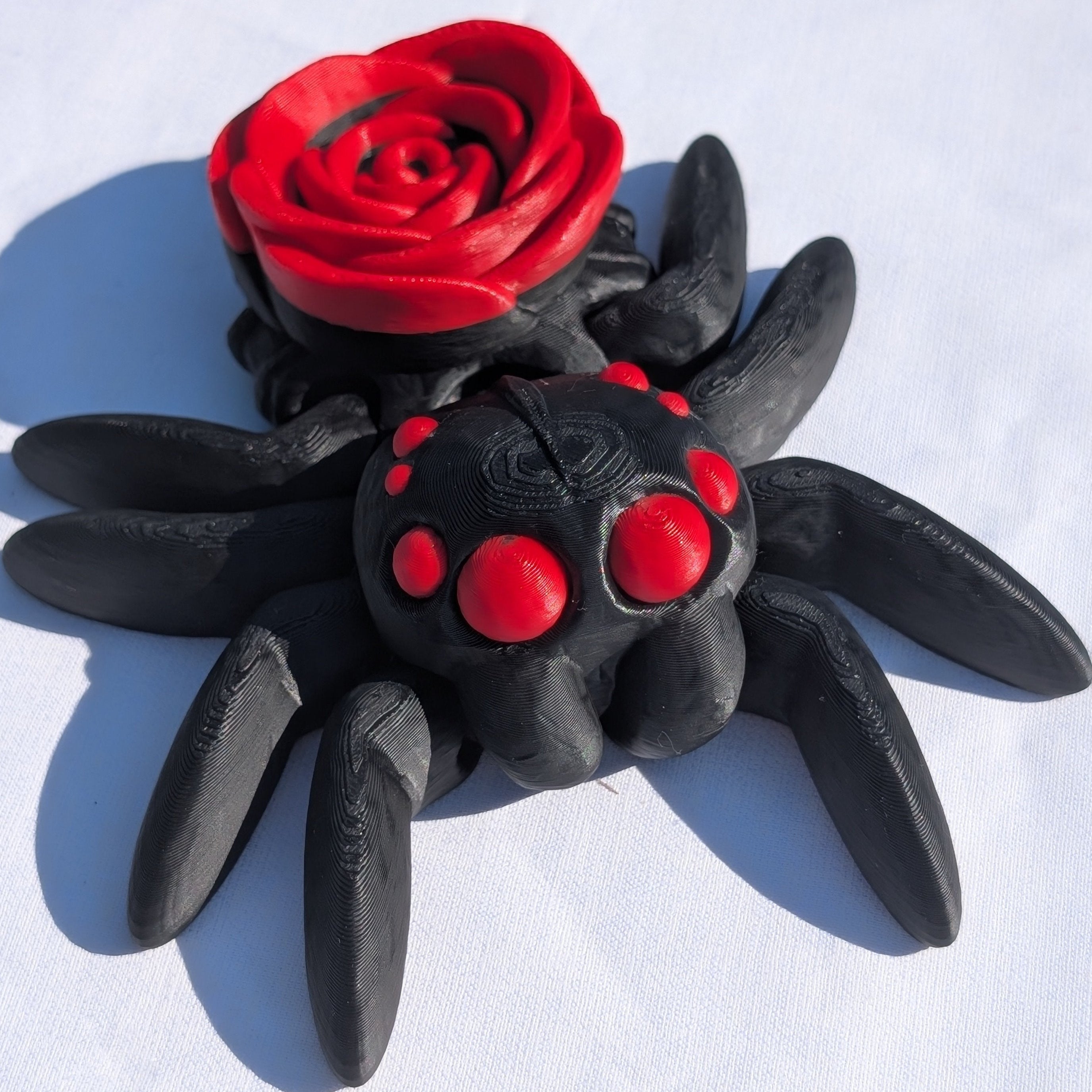 Black spider with red eyes and a red rose on a white background