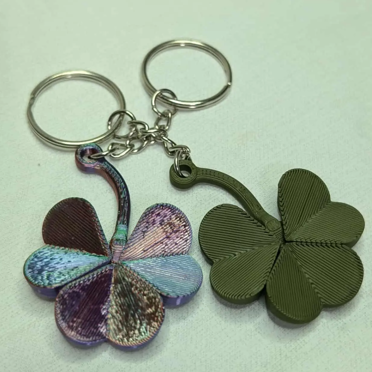 Two keychains shaped like four-leaf clovers on a light green background